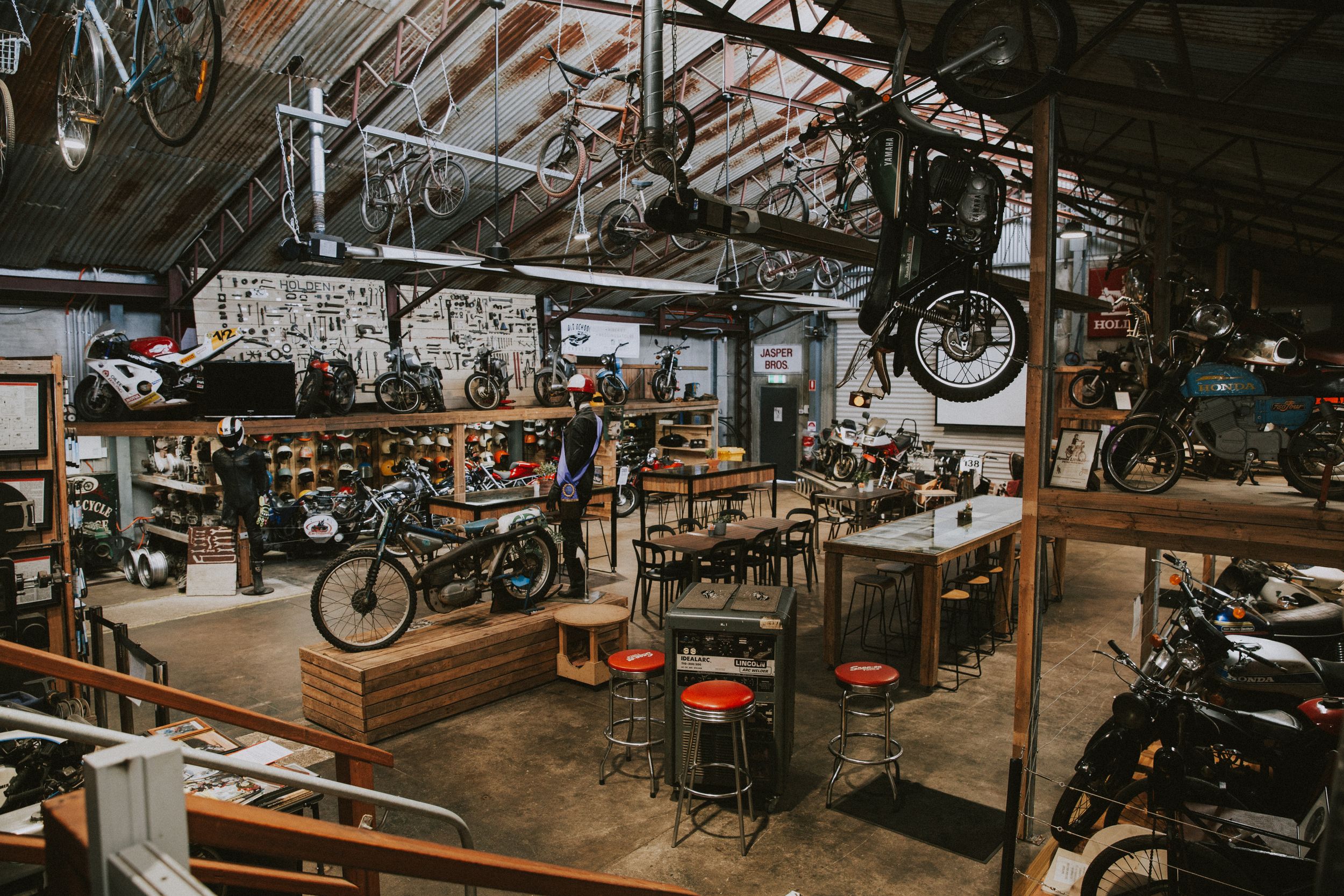 Vintage motorcycles and bicycles on display in a dimly lit industrial workshop with wooden beams and metal fixtures.
