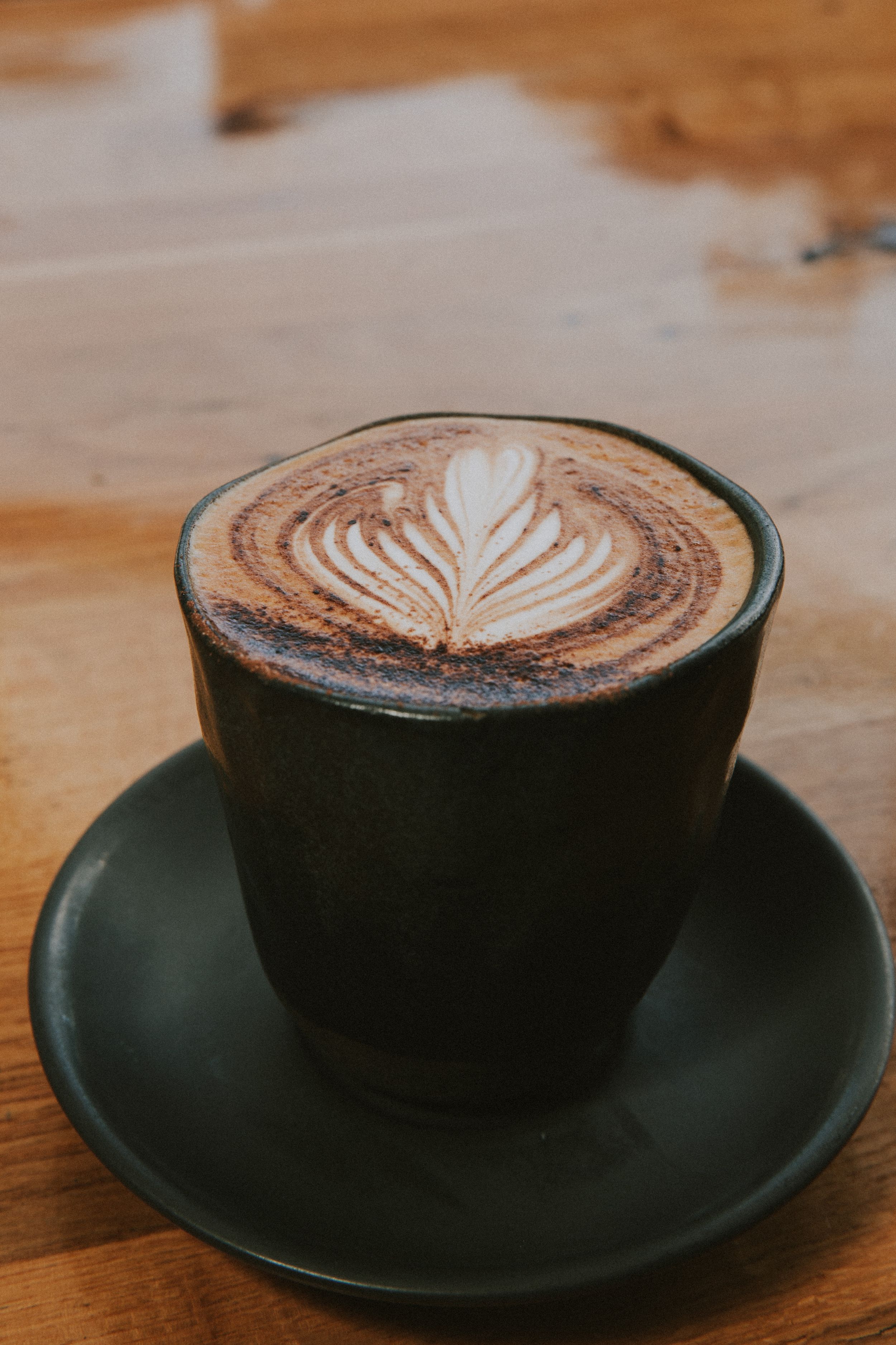 A black ceramic cup filled with hot chocolate or mocha coffee featuring an artistic leaf latte art design on wooden table.
