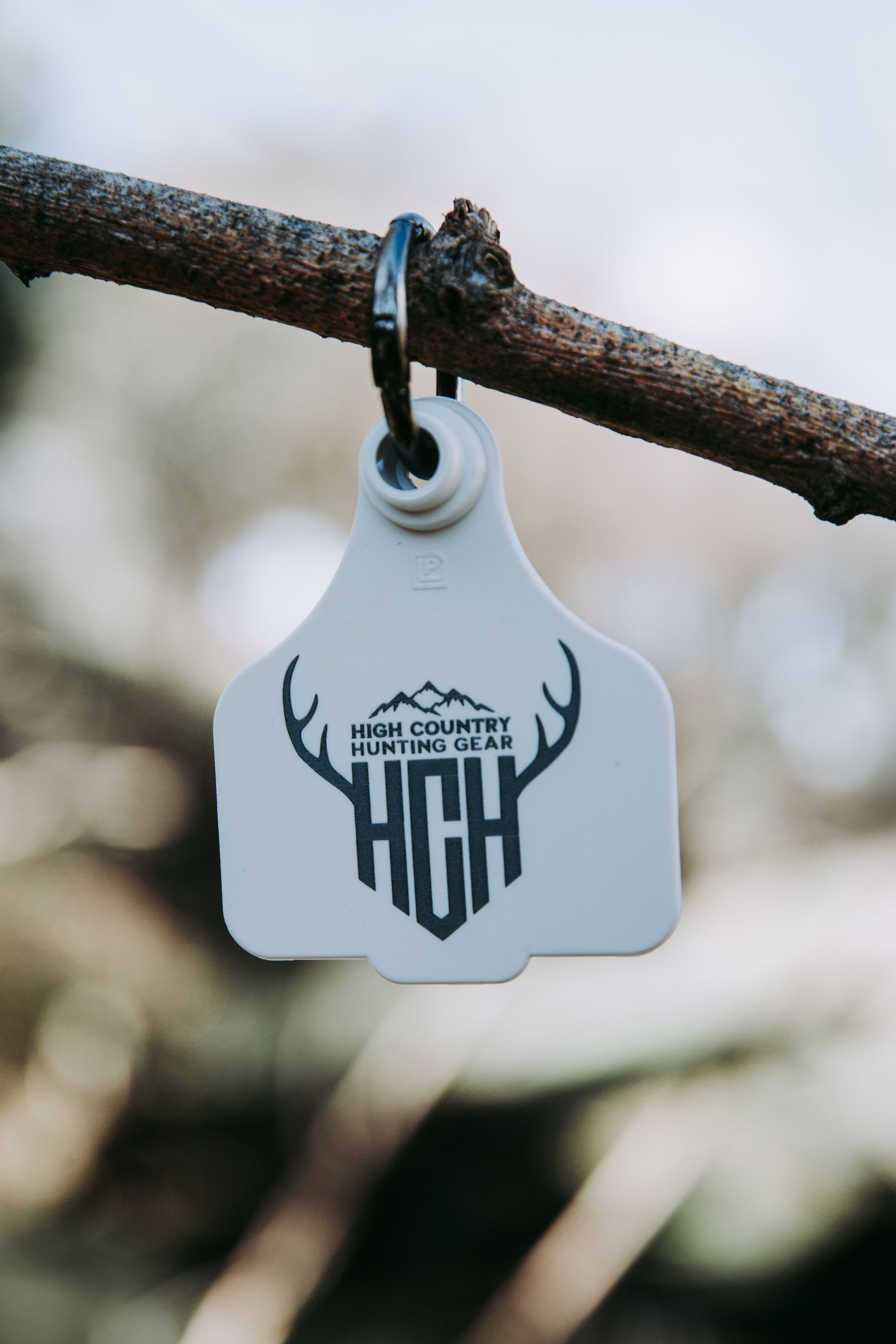 A series of white antler logo tags hanging from tree branches with a minimalist design in black text.