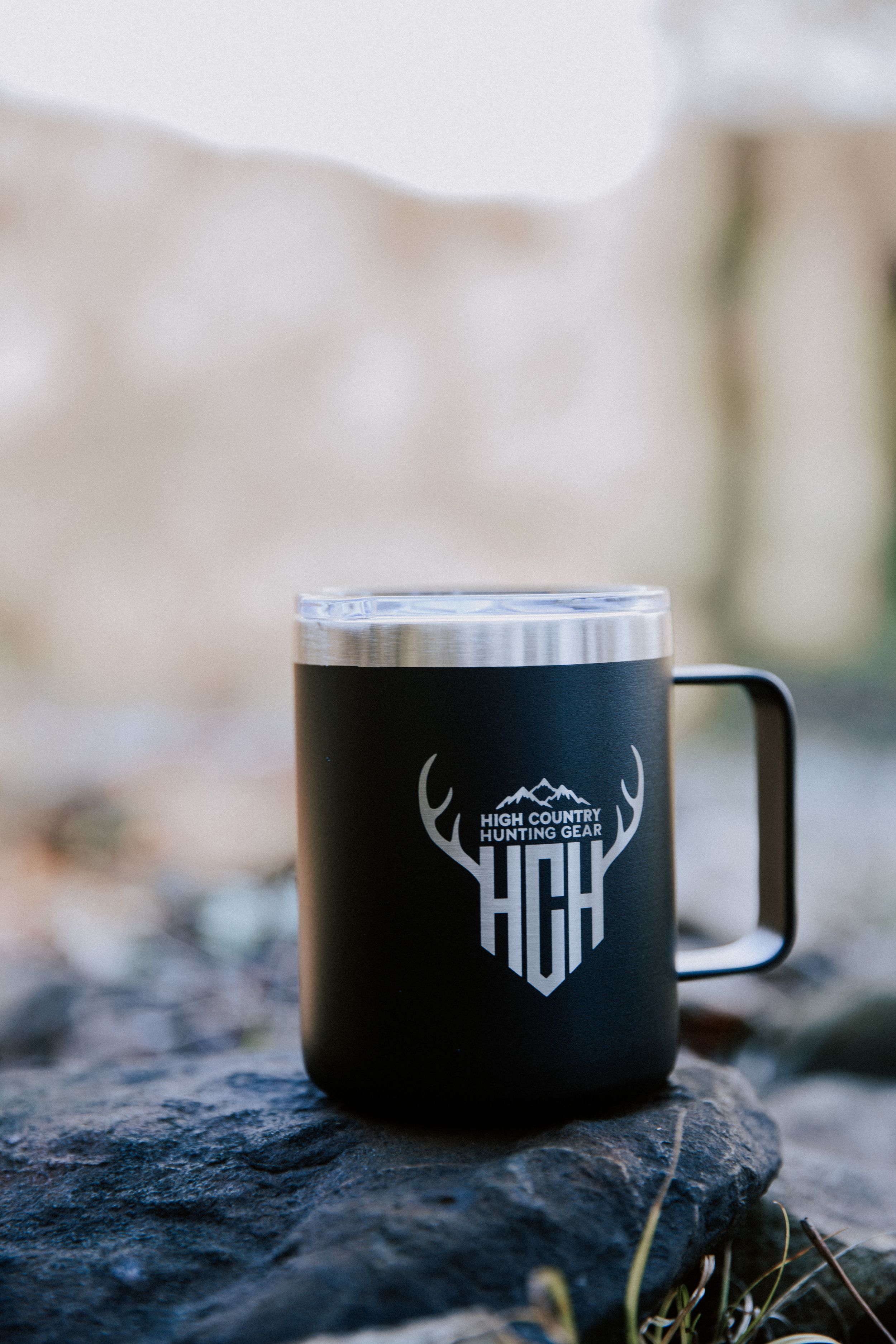 Black enamel camping mug with mountain logo shown in sequence of four similar shots on rocky outdoor surface.