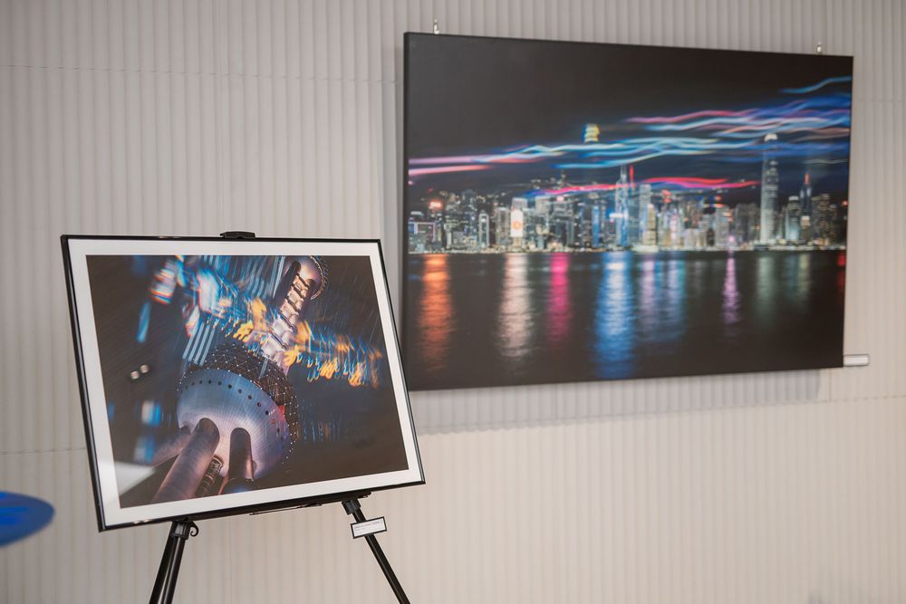 Gallery display featuring a large wall-mounted night skyline photograph beside a framed abstract city lights print on a black easel.