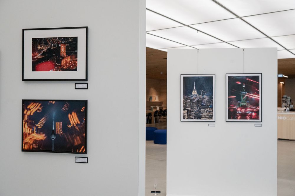 Gallery wall displaying framed night cityscape photographs with vivid red and orange tones in a bright, modern exhibition space.