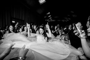 Black and white photo of a bride dancing joyfully surrounded by guests at a lively wedding reception.