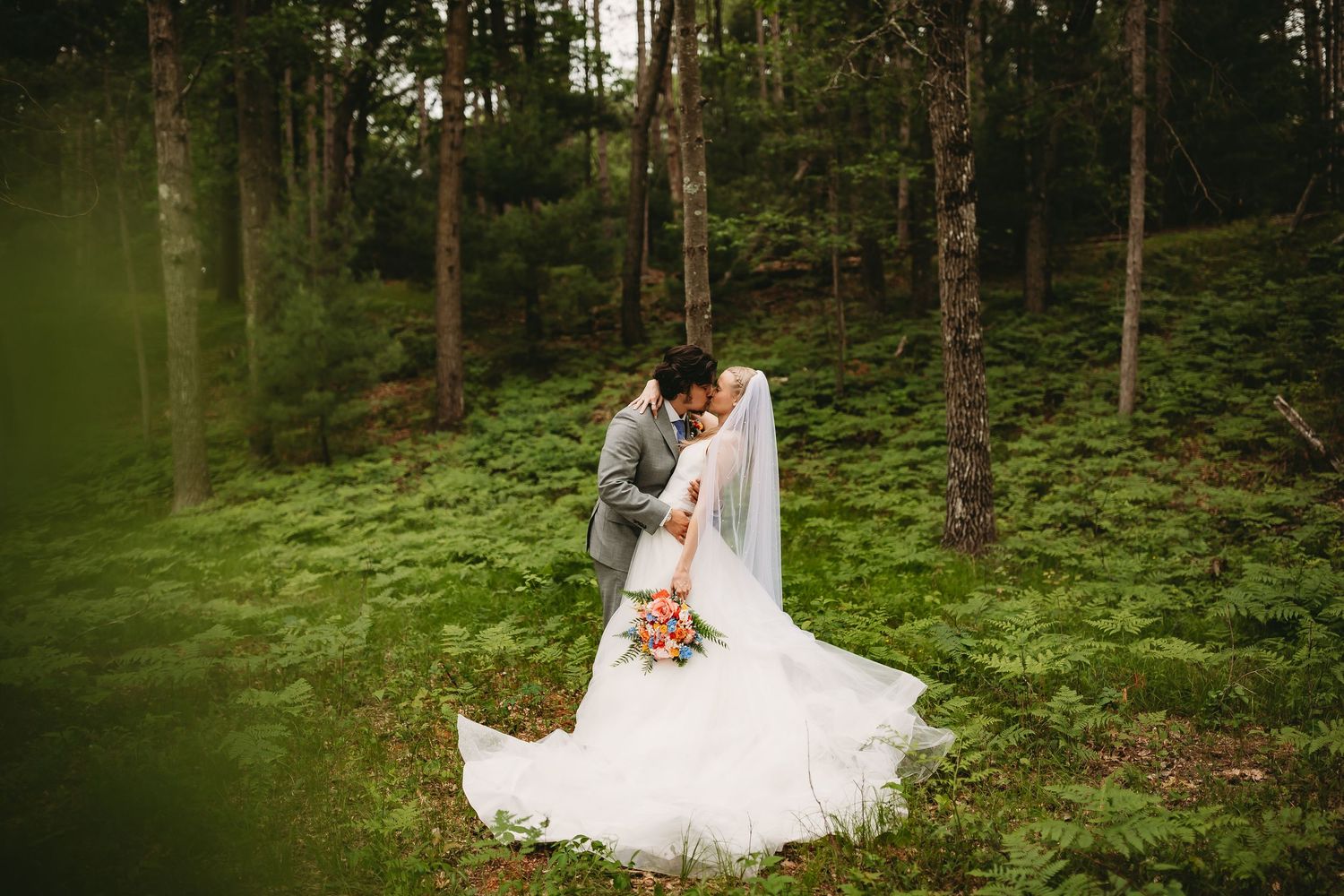 Bride and Groom kissing with a slight dip in a soft bed of ferns