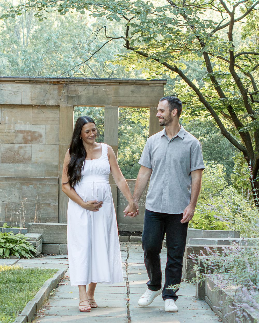 Pregnant mom and dad hold hands and walk through the garden in strongsville