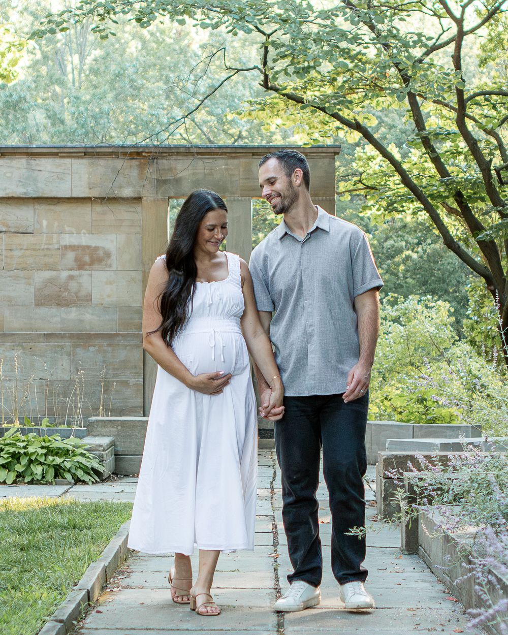 Pregnant wife and husband hold hands in the cultural gardens in strongsville