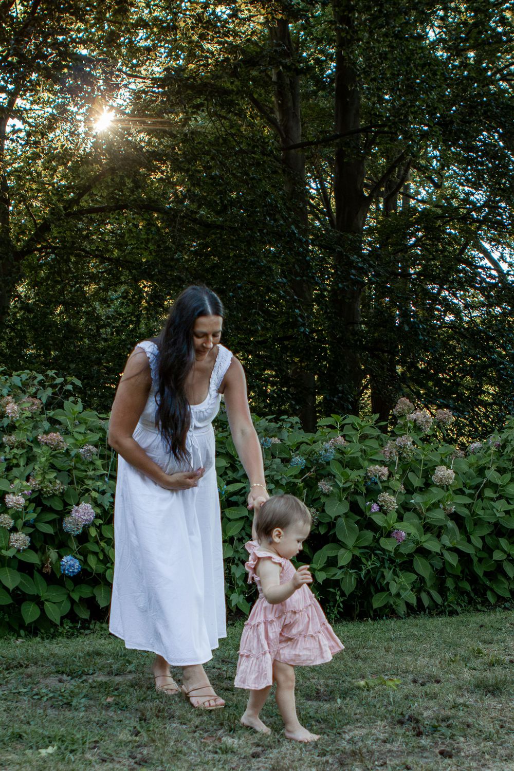 Mom holds pregnant belly and toddlers hand walking through a garden in Strongsville.
