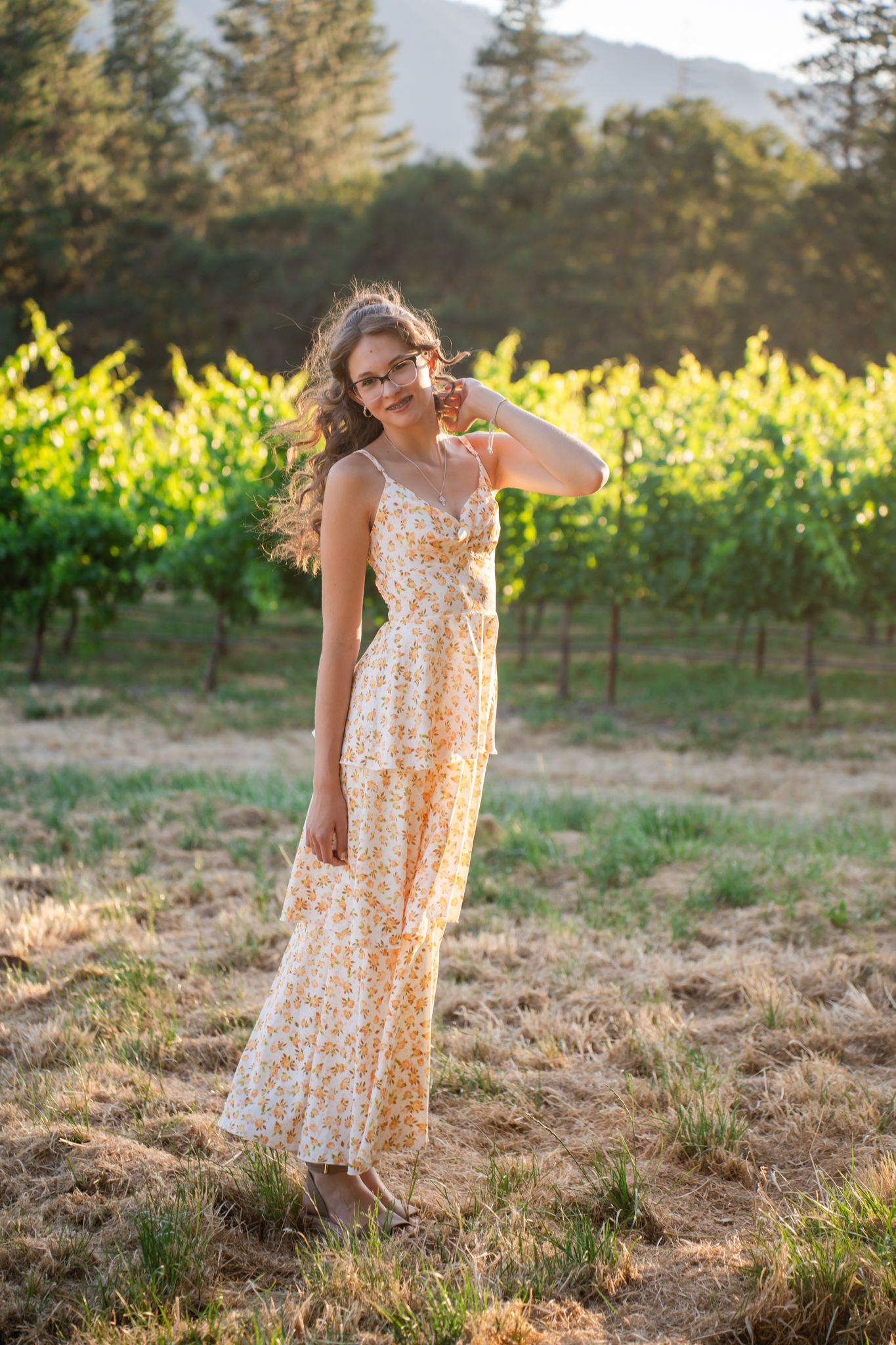 senior portrait of a girl in a field by a vineyard with golden hour light