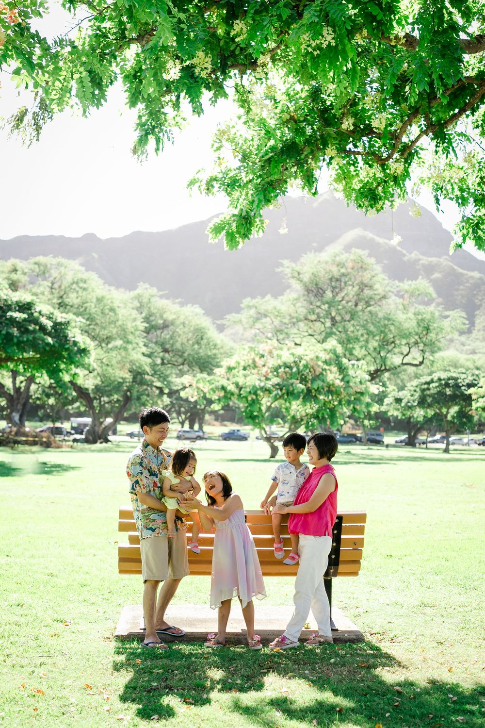 family of five gathered around a wooden bench in a lush green park with diamondhead  views in Hawaii.