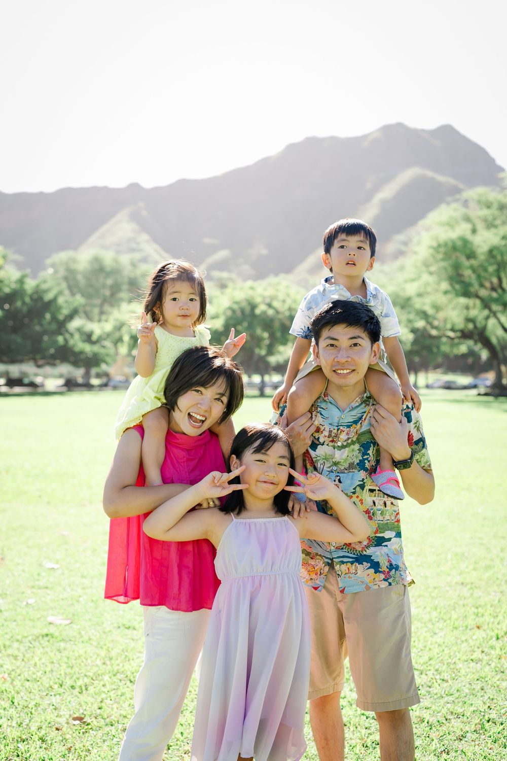 family of five posing outdoors on green grass with diamondhead in background on sunny day, kapiolani park in hawaii