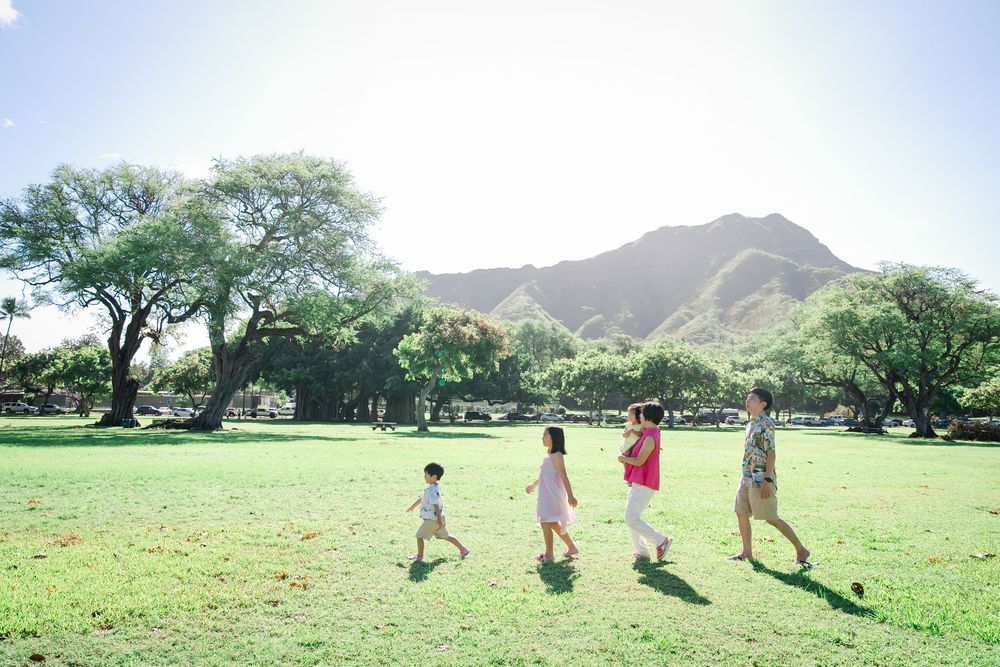 Family of four walking through a lush green park with Diamond Head crater in the background , kapiolani park in Hawaii.