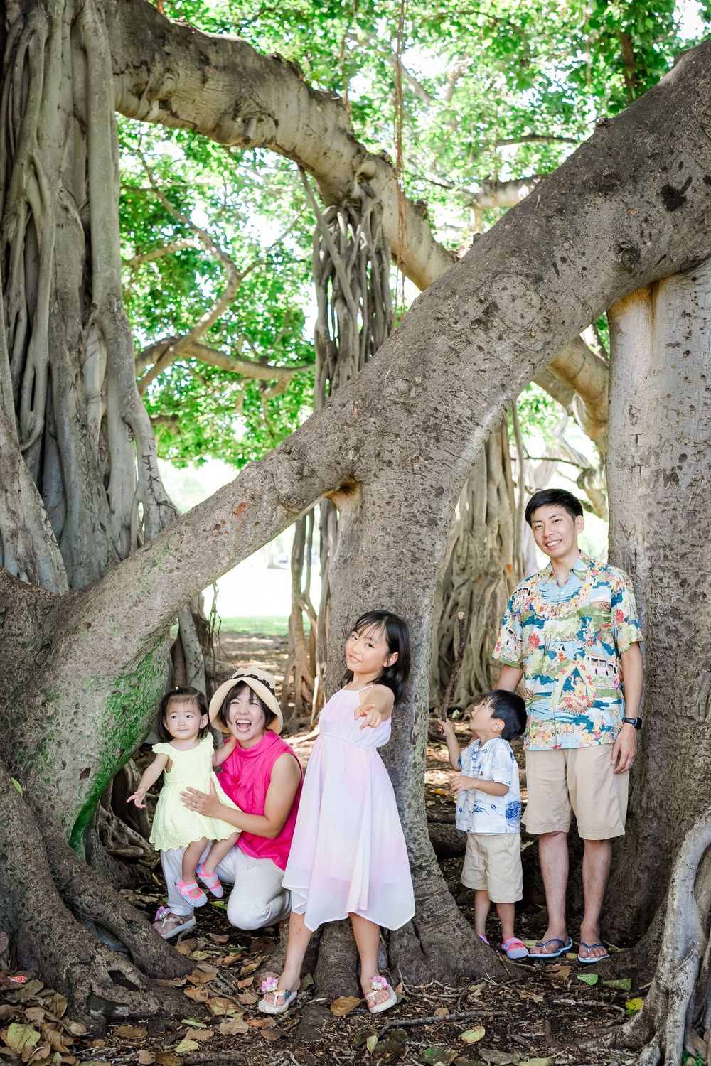 Family of five posing together inside a large banyan tree at Kapiolani Park in Honolulu, Hawaii