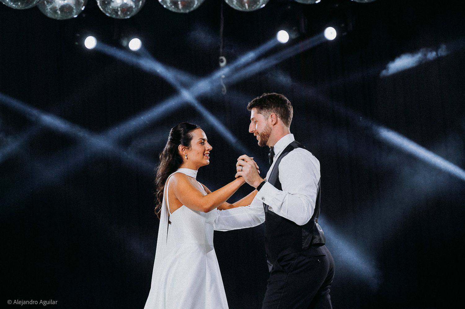 Couple shares first dance at wedding reception under dramatic stage lighting and mirror ball.