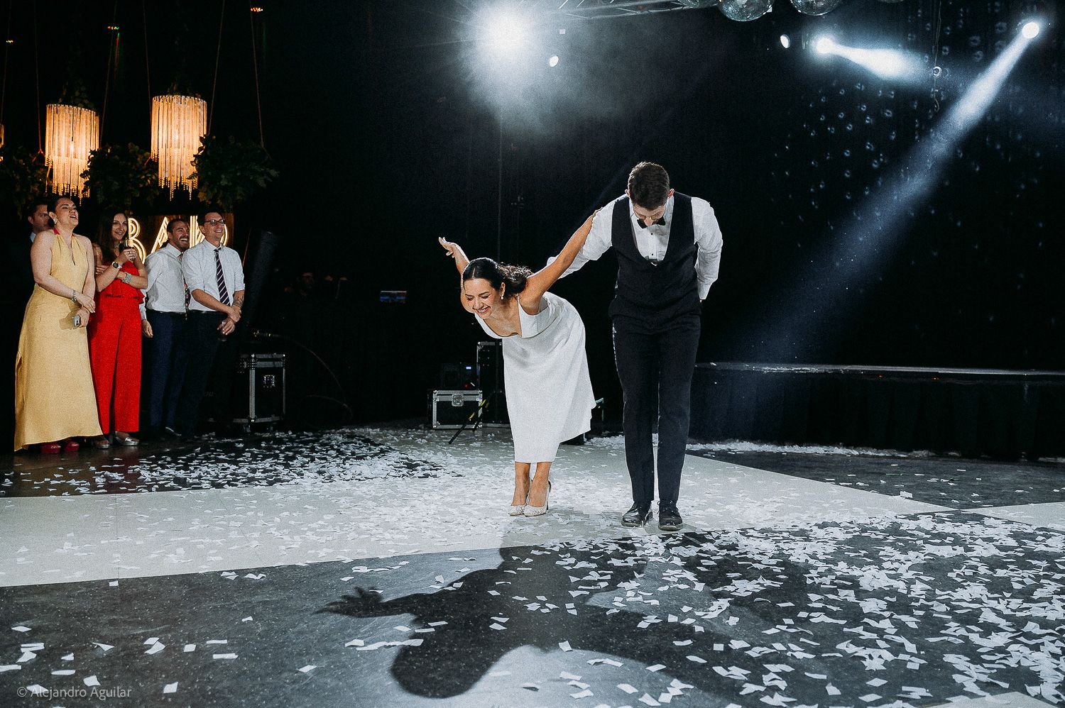 Bride and groom share first dance on confetti-covered floor at elegant wedding reception with guests watching.