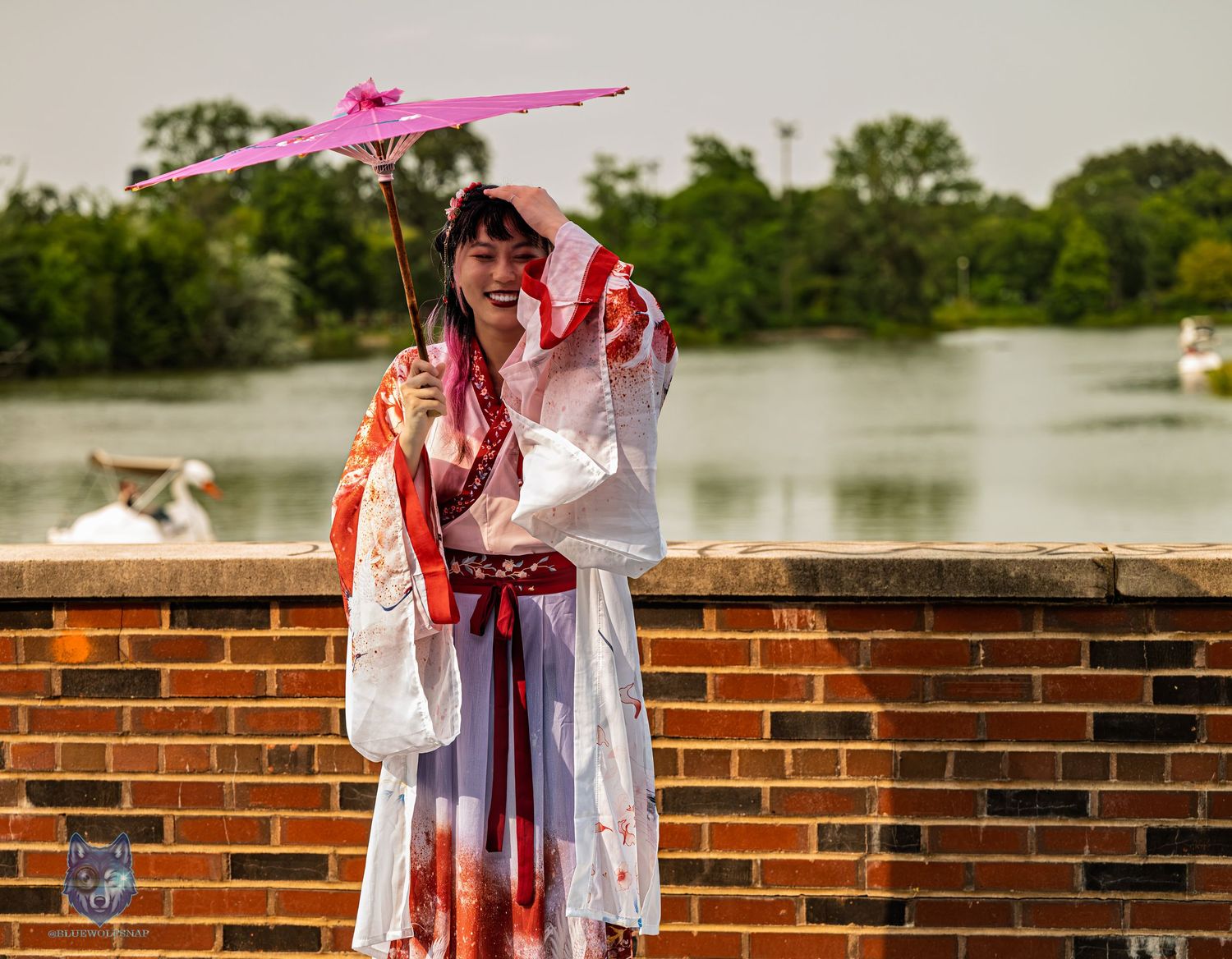 Woman in white and red Hanfu costume laughs while holding pink parasol near brick wall and lake. Chi.Shooters meet yutonew