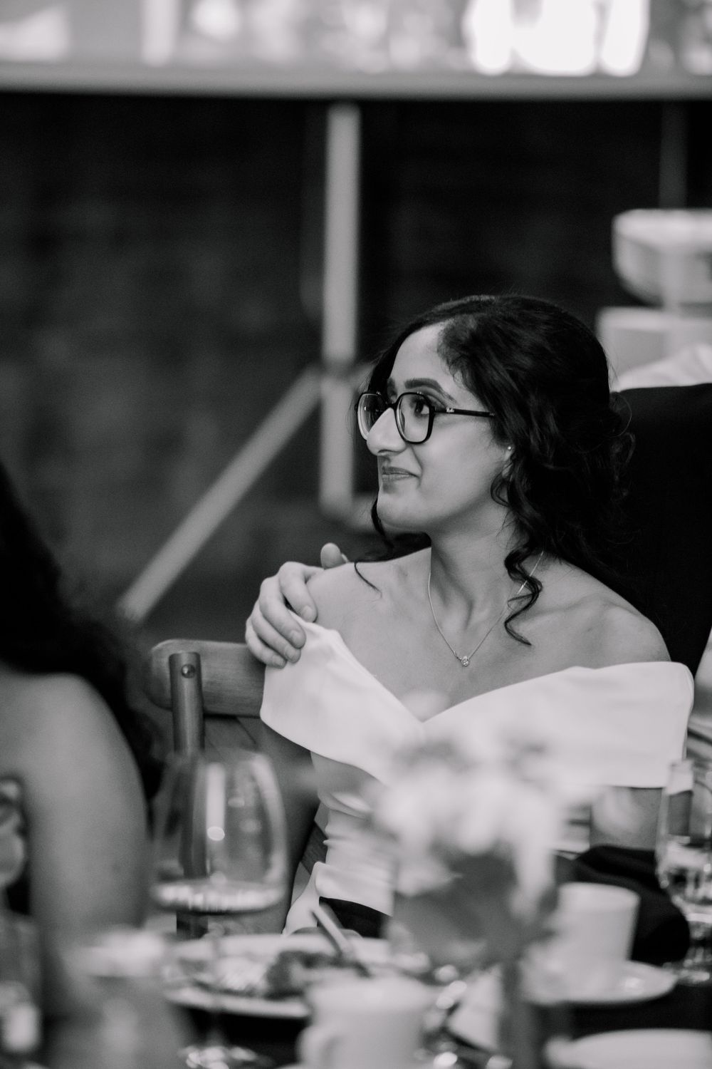 Black and white photo of a woman wearing glasses at a formal dinner, smiling and holding a napkin.