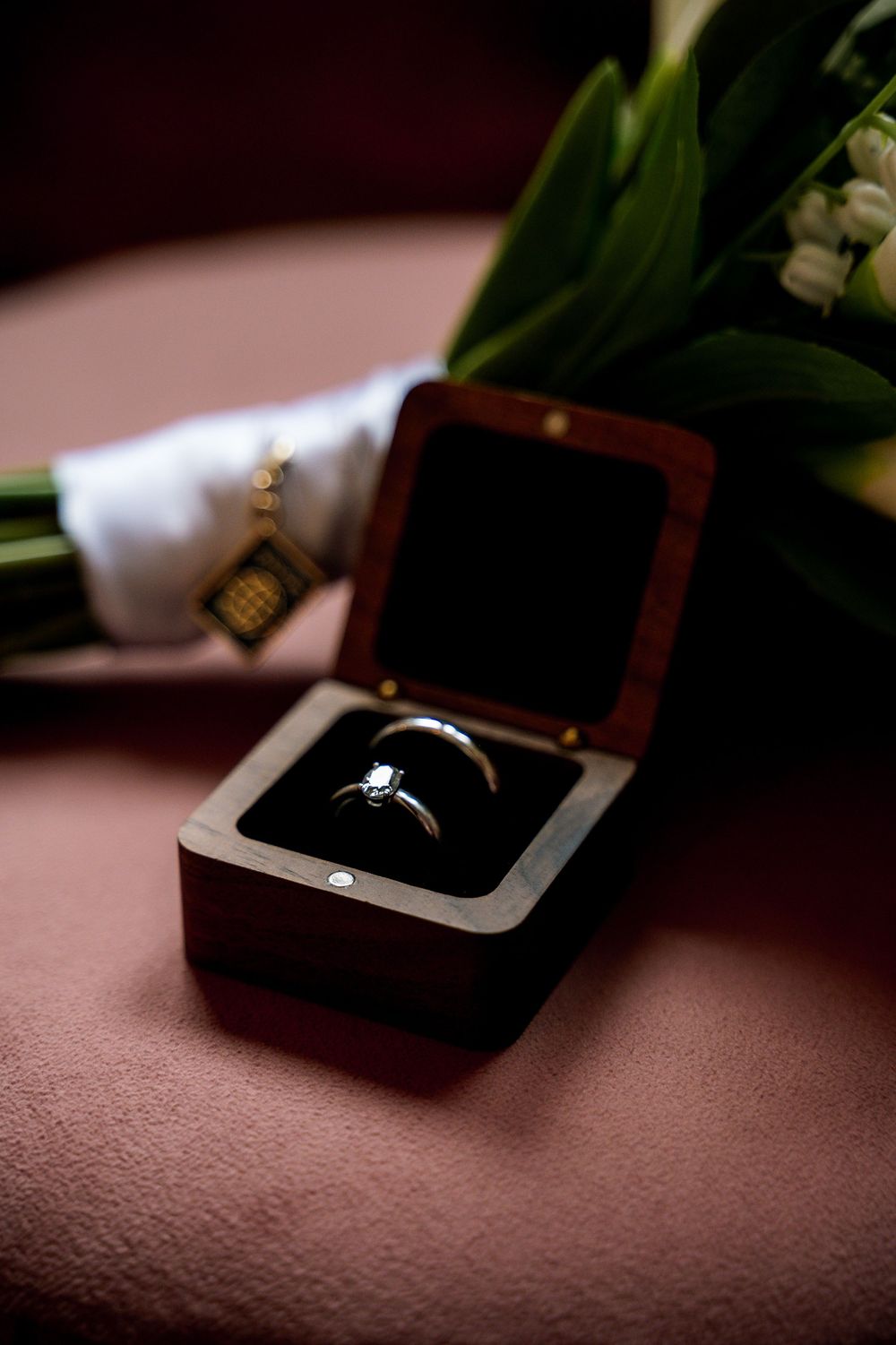 Diamond engagement ring in wooden box with flower bouquet backdrop.