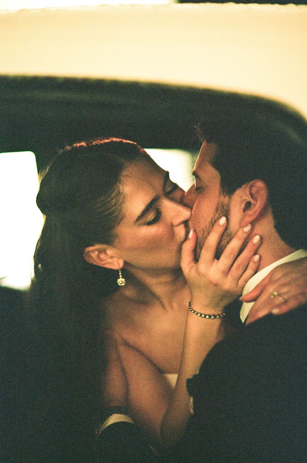 Couple sharing a romantic kiss inside a car, bride wearing elegant earrings and bracelet on their wedding day.