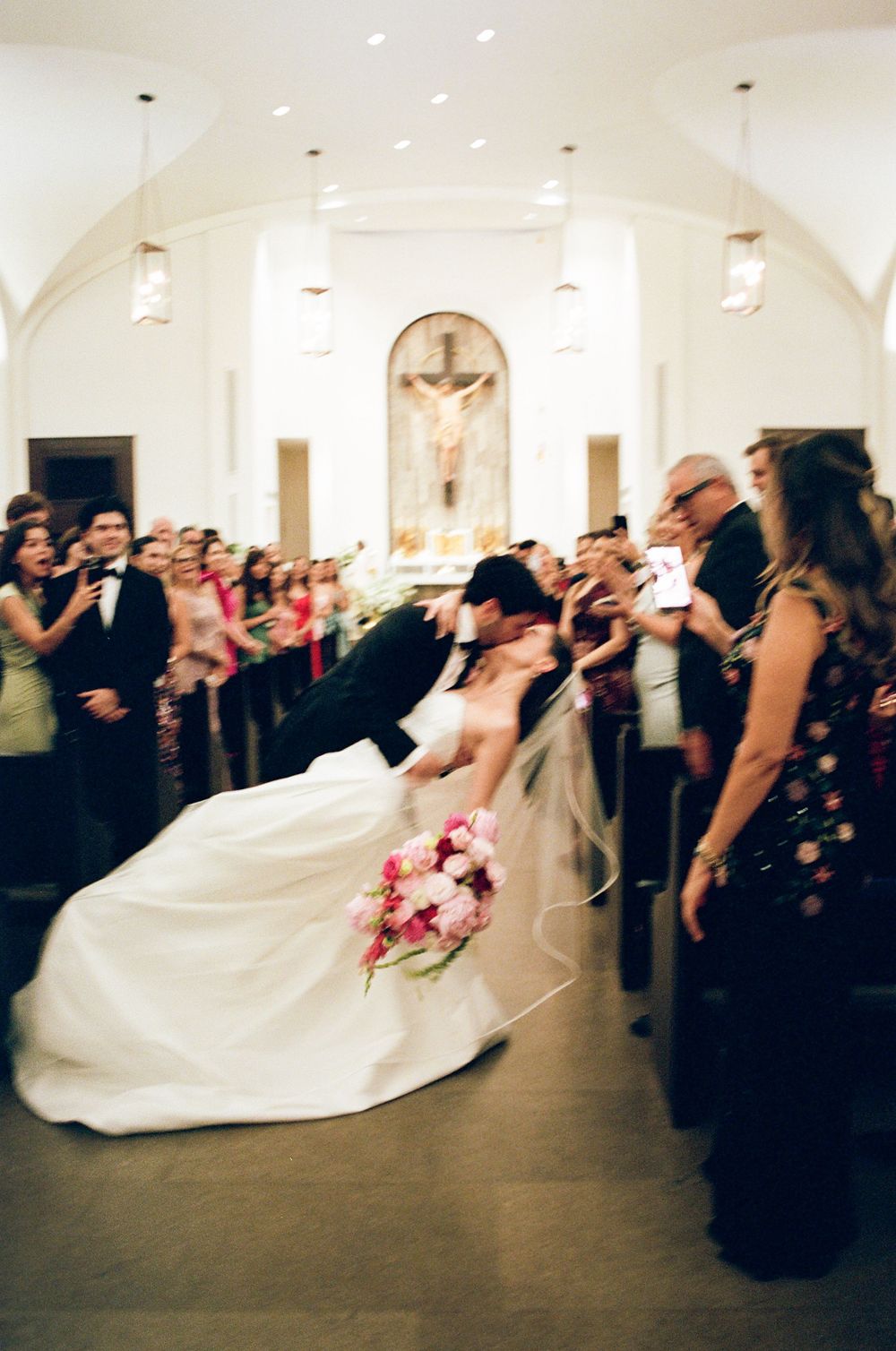 Bride and groom share a romantic dip kiss at the altar of a beautiful church surrounded by wedding guests.