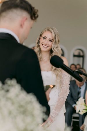 Smiling bride in lace wedding dress exchanges vows with groom at elegant outdoor ceremony.