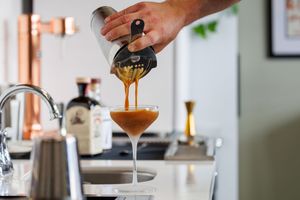 Bartender pouring an espresso martini cocktail from a shaker into a stemmed glass in a modern bar.