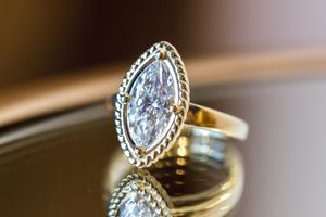 Gold ring with large marquise-cut diamond in bezel setting, reflecting on glossy surface.