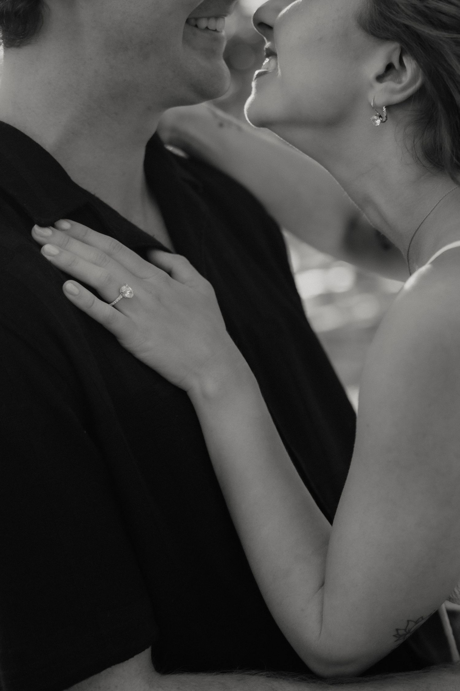 Black and white photo of engaged couple embracing, woman showing diamond engagement ring on her hand.