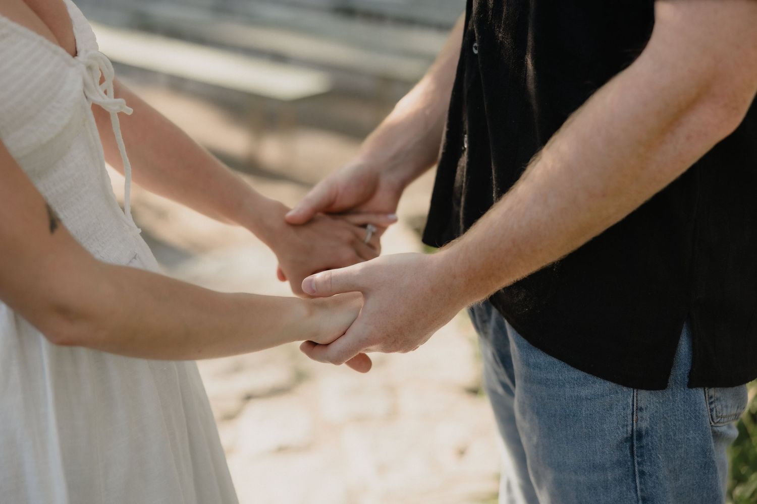 Couple holding hands tenderly in wedding attire, bride in white dress and groom in black shirt and jeans.