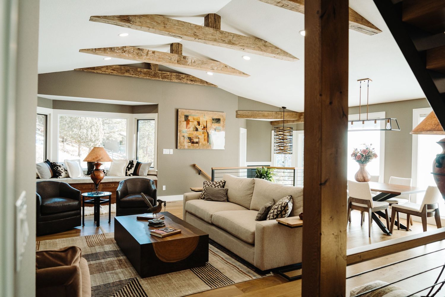 Spacious open-concept living room with vaulted ceilings, rustic wood beams, neutral sofas, and a connected dining area.
