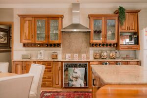 Warm wooden kitchen cabinets with glass doors, stainless steel range hood, wine rack, and granite countertops.