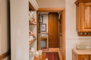Hallway view into a wood-paneled closet with dresser, framed art, and red rug through an open doorway.