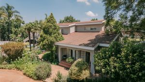 Aerial view of a charming two-story home with terracotta roof tiles surrounded by lush green trees and gardens.