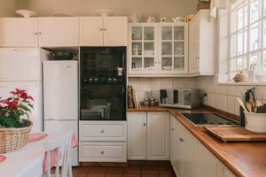 White kitchen with wooden countertops, glass-front cabinets, black oven, white fridge, and terracotta tile floors.