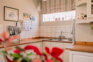Bright kitchen corner with white cabinets, wooden countertops, stainless steel sink, tiled backsplash, and striped Roman blind window.