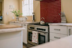 Modern kitchen with white cabinets, stainless steel range cooker, red tile backsplash, and kettle on hob.