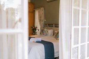 Elegant bedroom viewed through white French doors, featuring a neatly made bed with blue accents and floral pillows.