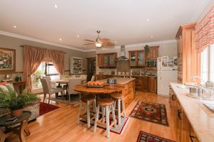 Spacious open-plan kitchen and dining area with wooden cabinets, island with bar stools, hardwood floors, and warm natural lighting.