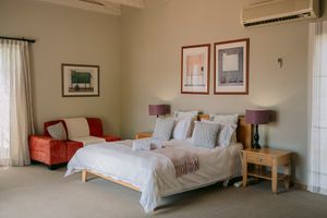 Bright hotel bedroom with white bedding, red armchair, wooden nightstand, purple lamps, and framed art above the bed.