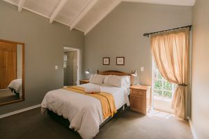 Bright bedroom with vaulted ceiling, queen bed, yellow accents, wooden furniture, and French doors with sheer curtains.