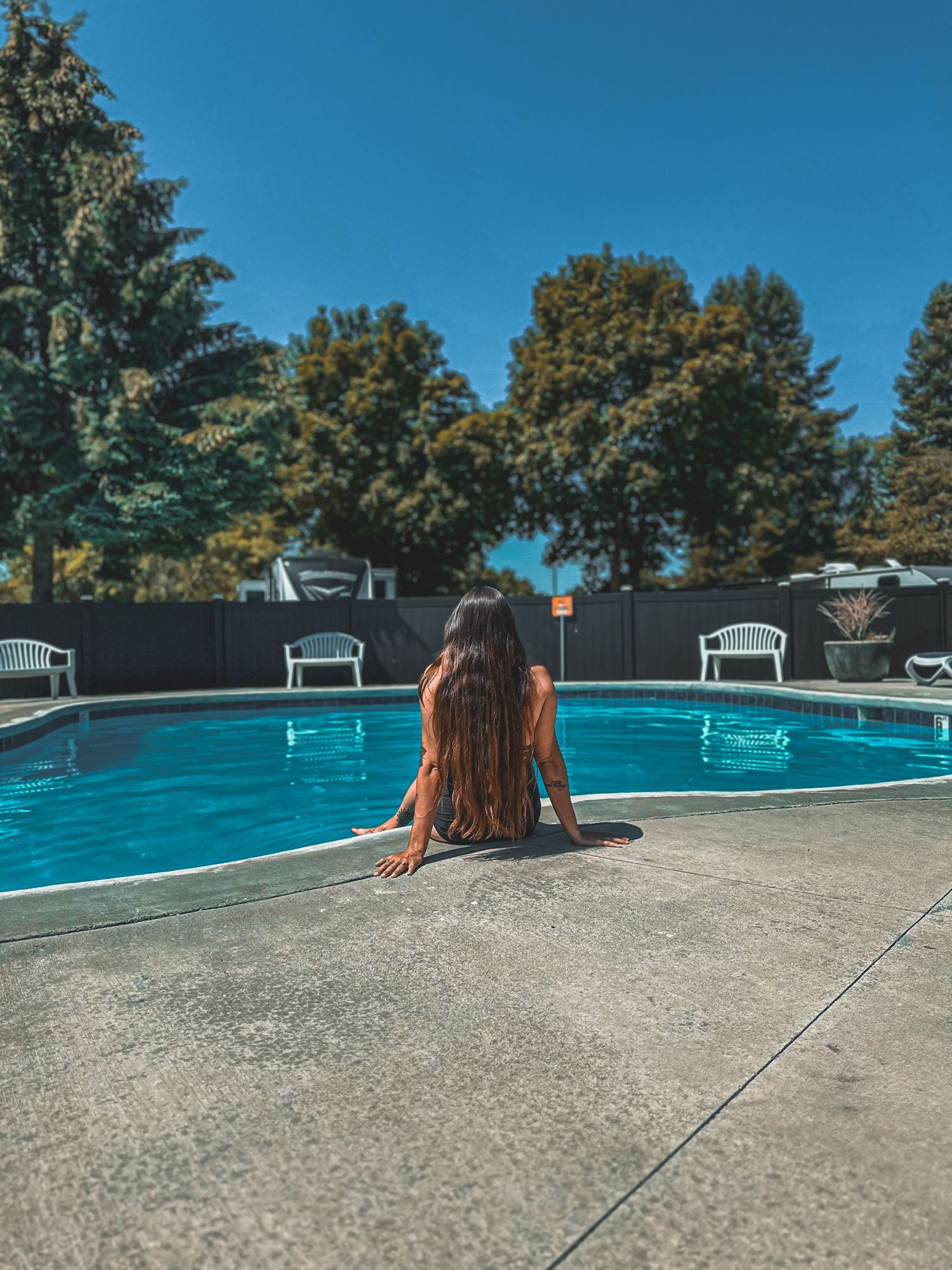 Woman with long dark hair relaxing at edge of outdoor swimming pool.