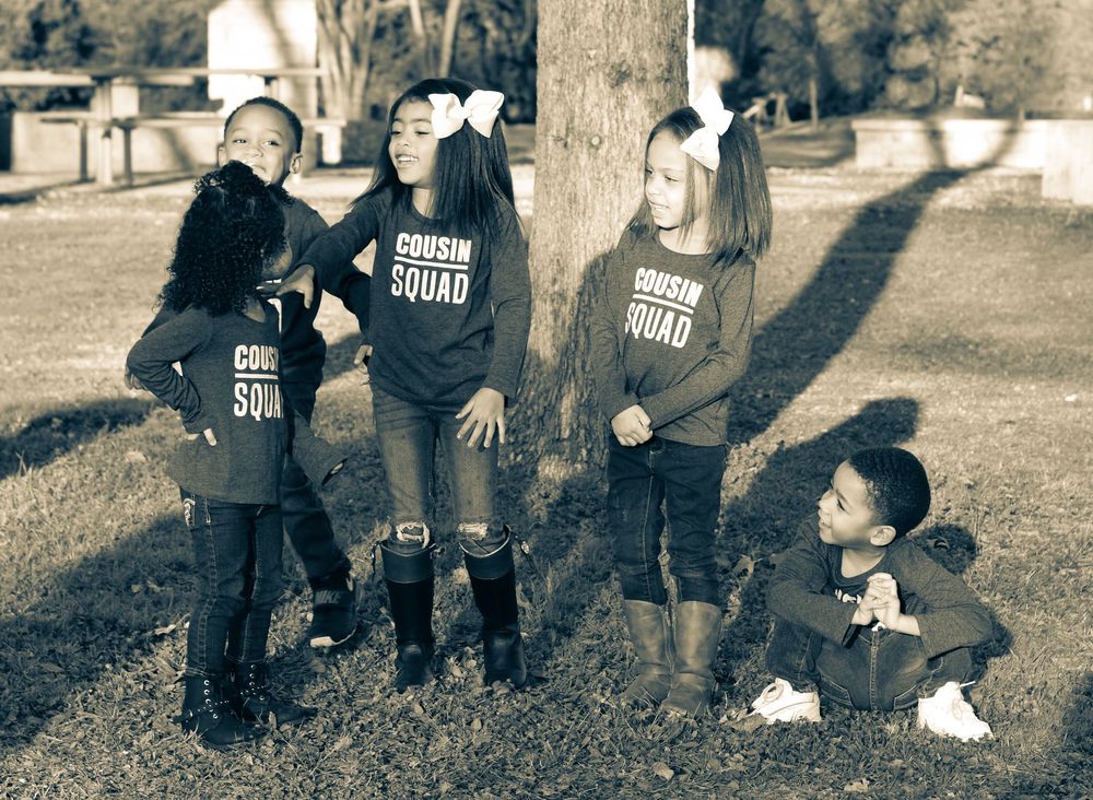 Four children in Cousin Squad shirts posing playfully around a tree in sepia tone photo.