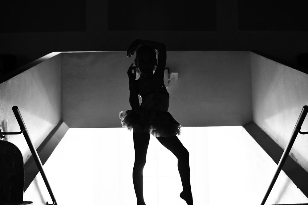 Silhouette of a ballerina in a tutu posed gracefully in black and white dramatic lighting.