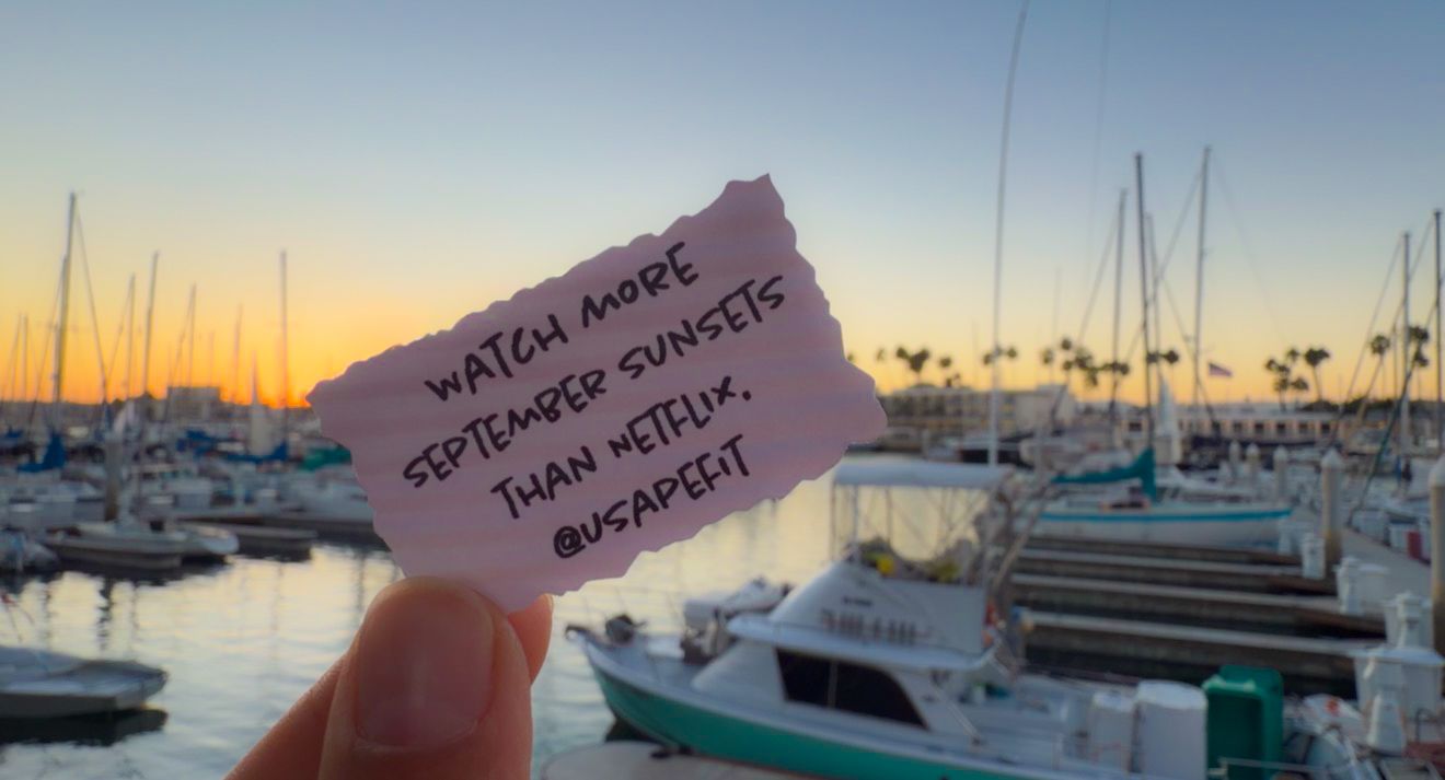 Hand holding a note at a marina sunset reading watch more September sunsets than Netflix @usademi.