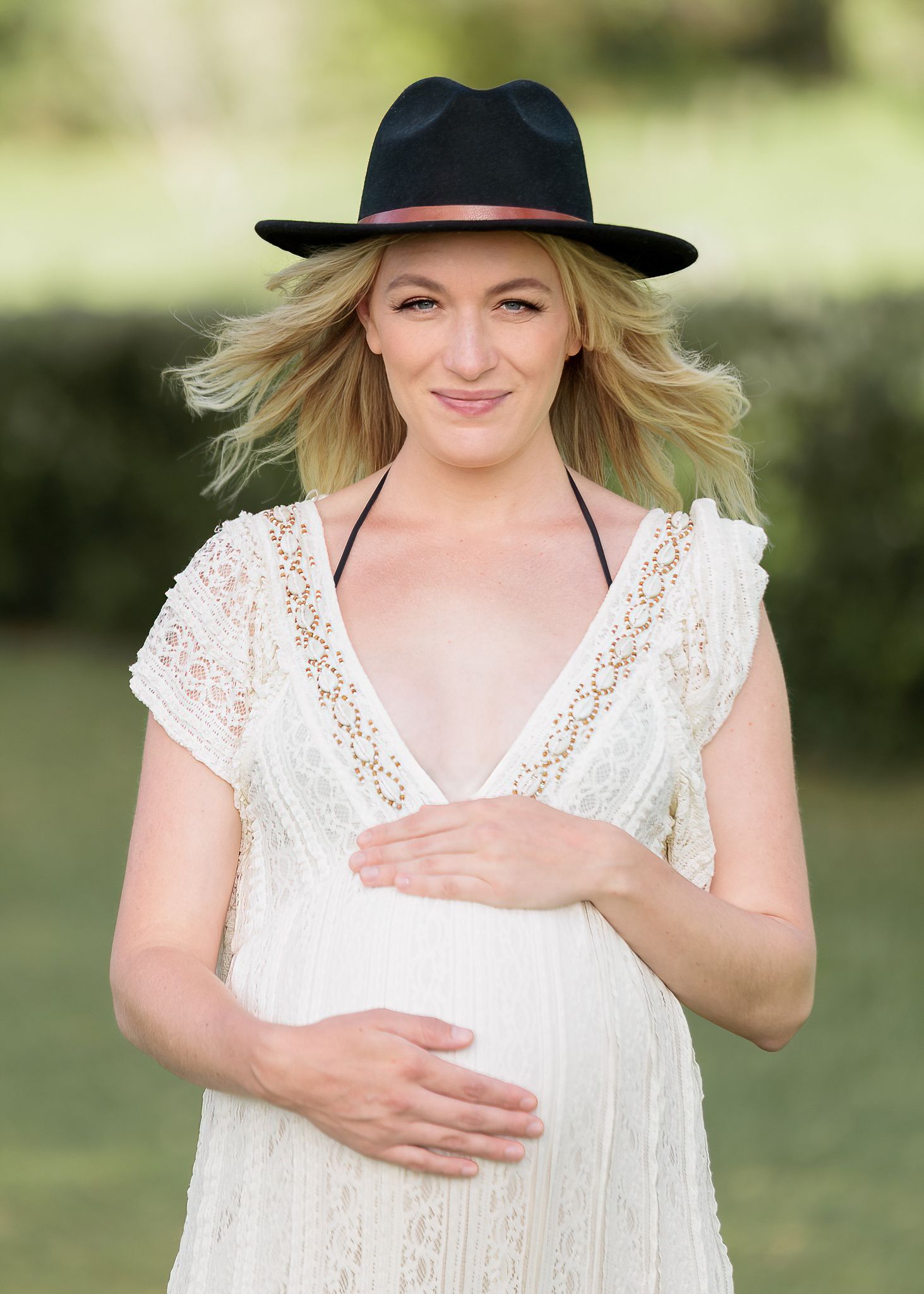 Outdoor portrait of a pregnant woman in a white lace dress and black hat