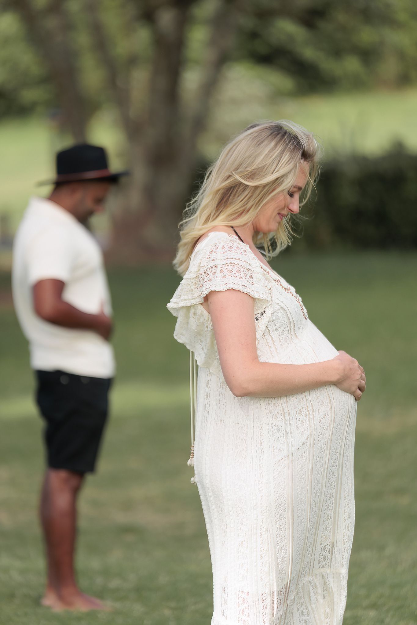 Humorous maternity portrait of a pregnant woman holding her bump while her partner mirrors the pose in the background