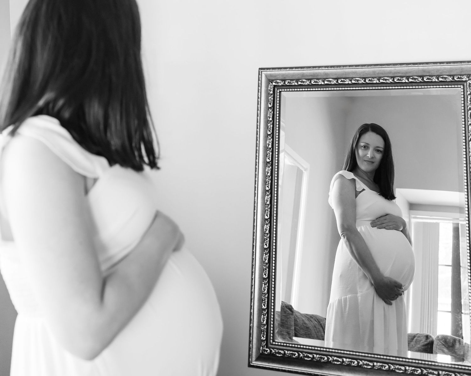Black and white maternity portrait of a pregnant woman admiring her reflection in a framed mirror