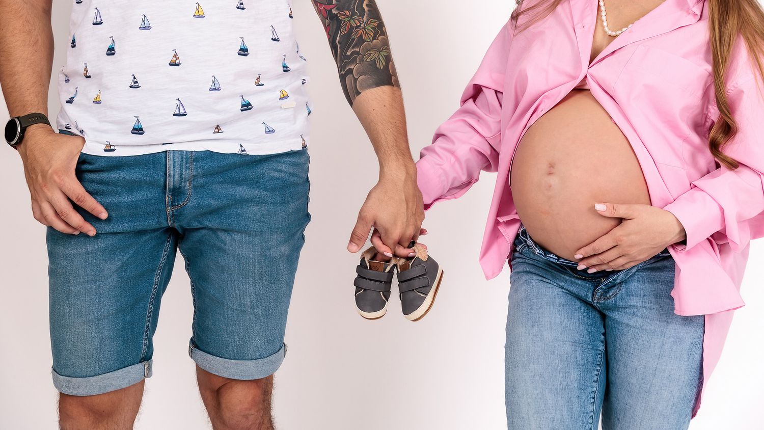 Expectant couple holding tiny baby shoes together in front of the mother’s bump