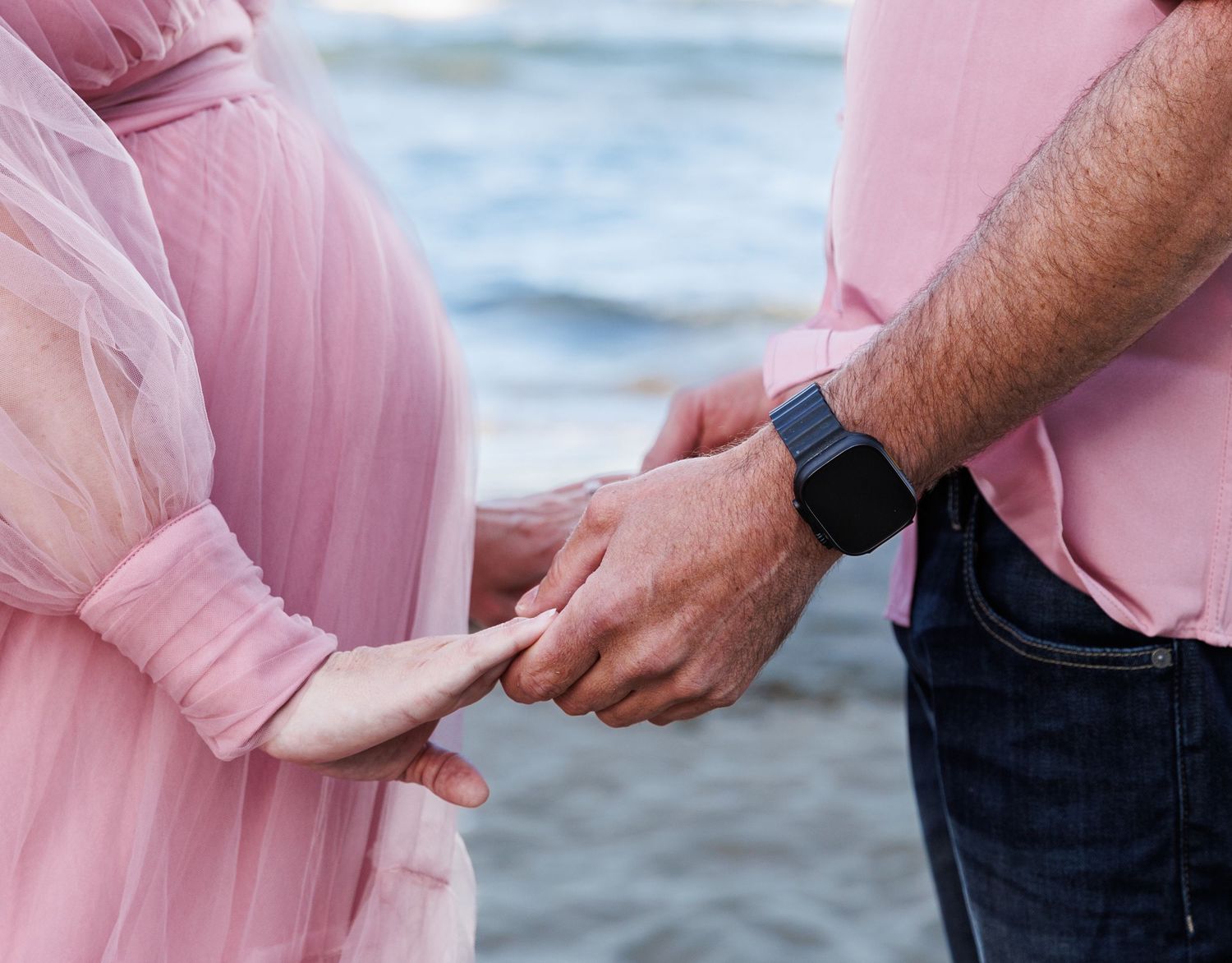 Close-up of an expectant couple holding hands beside the mother’s baby bump at the beach