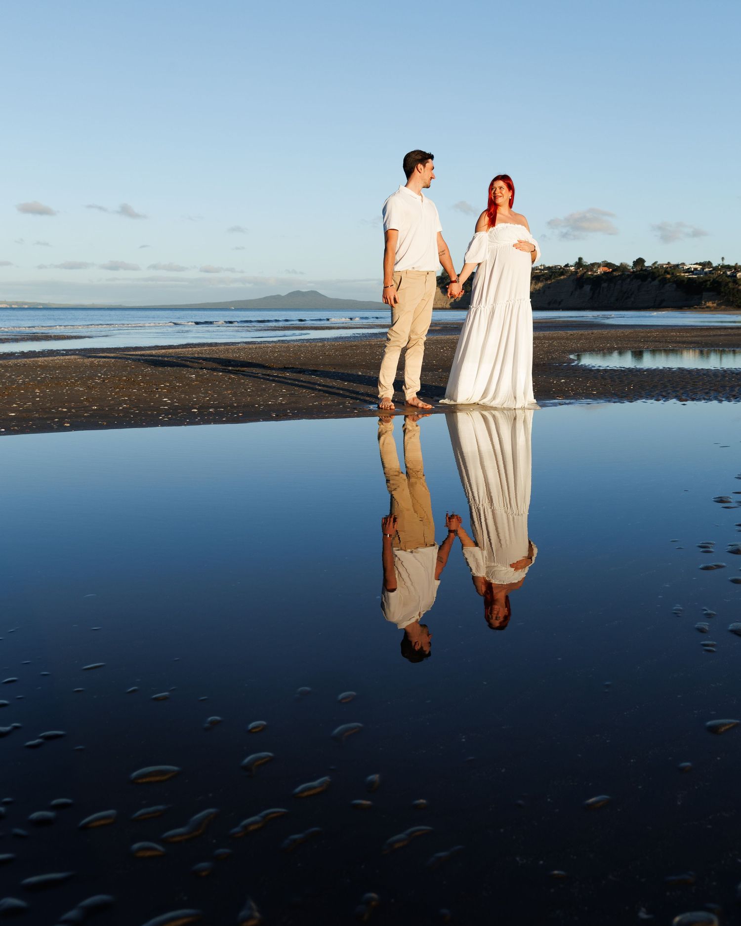 Maternity couple at sunset on Long Bay Beach with their reflection visible in the shallow water