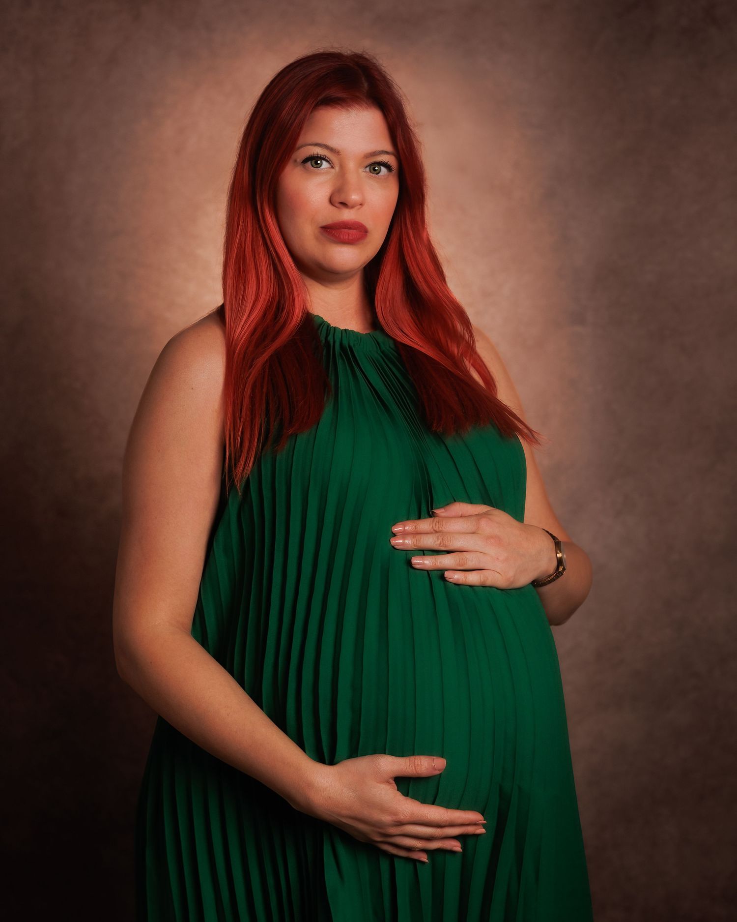 Pregnant woman in a green dress posing with one hand on her baby bump during a studio maternity session
